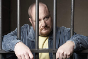 Bald mid-adult man standing behind prison bars