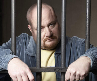 Bald mid-adult man standing behind prison bars