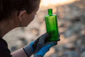 Mudlark-Monika-Buttling-Smith-in-gloves-examines-an-old-green-glass-bottle-with-embossed-text-C2A9-London-Museum