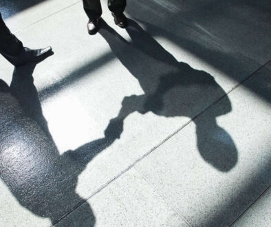 A shadow on a tiled floor of two businessmen shaking hands.