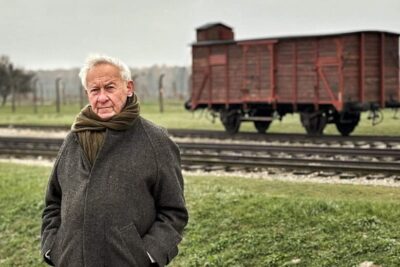 2.-Simon-Schama-standing-in-front-of-a-train-carriage-at-Auschwitz-Birkenau-2400x1350